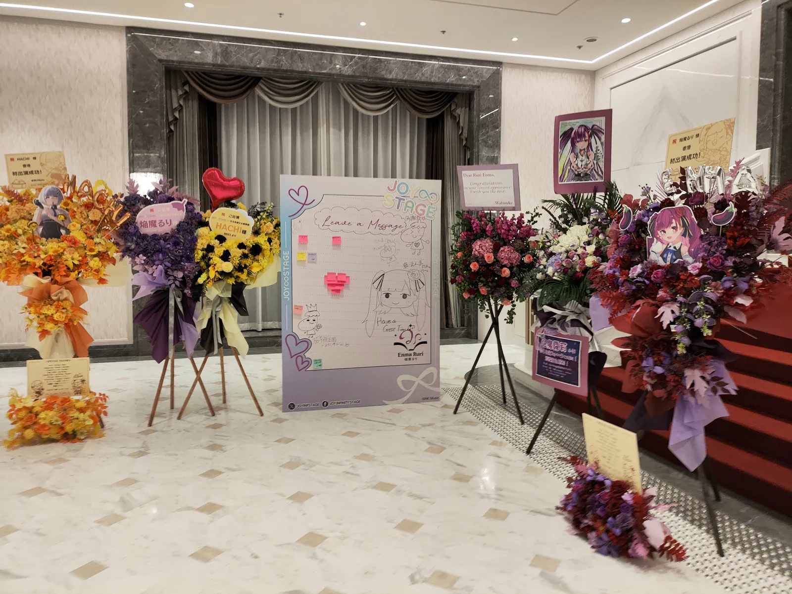The Joy∞ Stage lobby with flower stands for each performer in orange, purple and yellow, and a message board reading Leave a Message