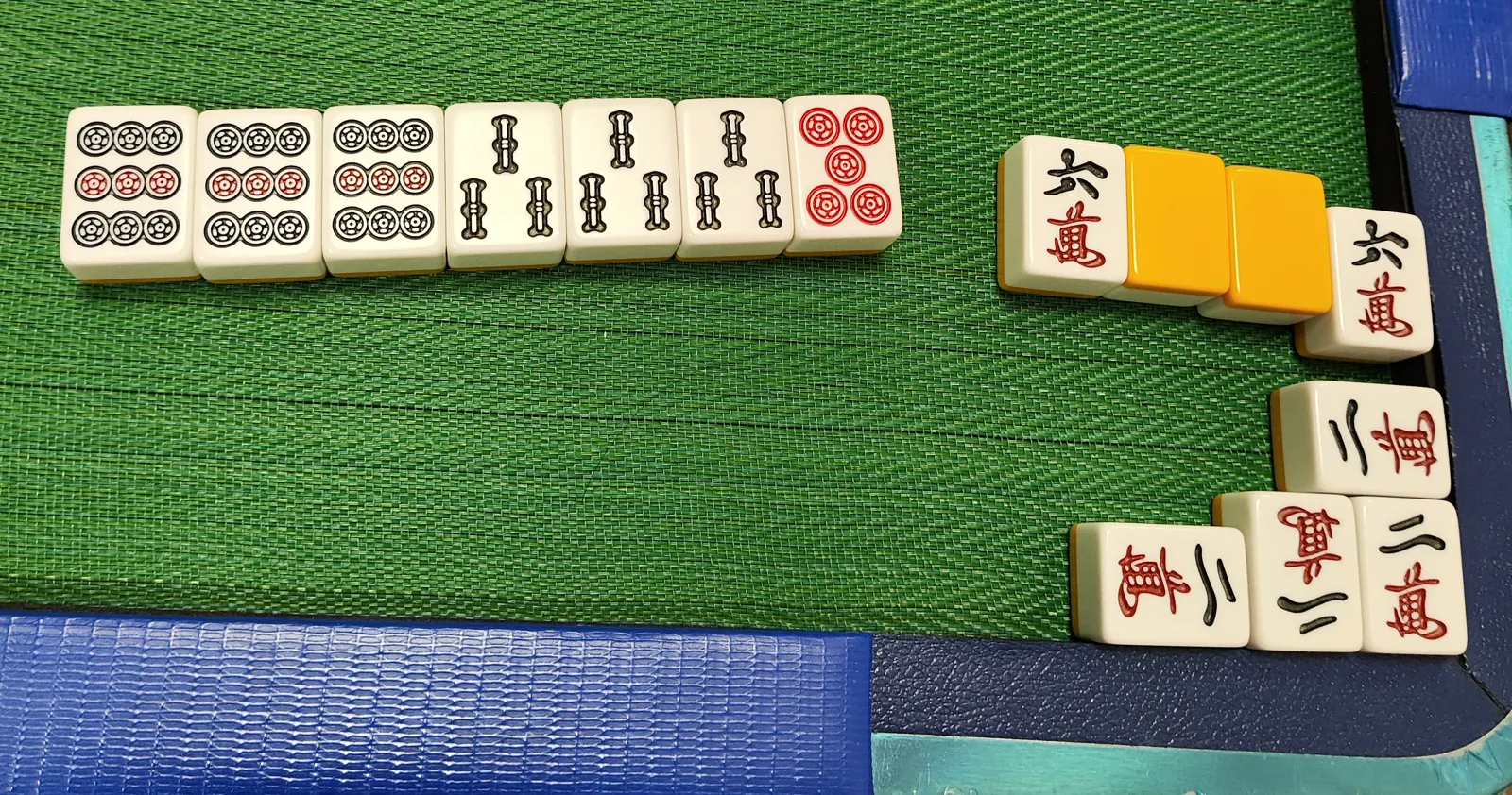 A finished riichi hand laid out on a green table, with 9-pin and 1-sou tiles to the left and man tiles plus two face-down orange tiles to the right